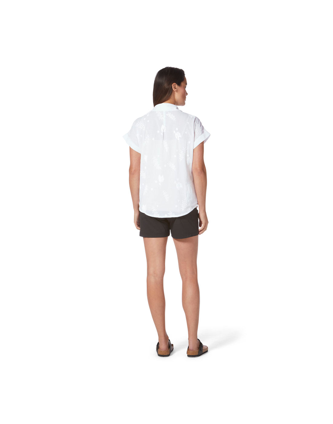 Back view of a woman wearing the Royal Robbins Women's Oasis Shirt in white with black shorts and sandals.