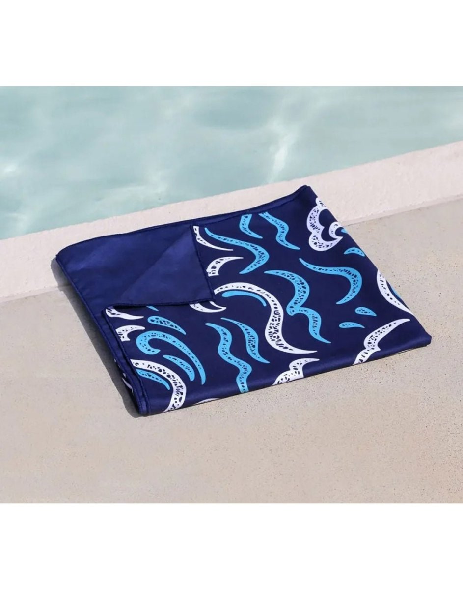 The K5 Microfibre Beach Towel, blue and white, sits folded by the pool’s edge.