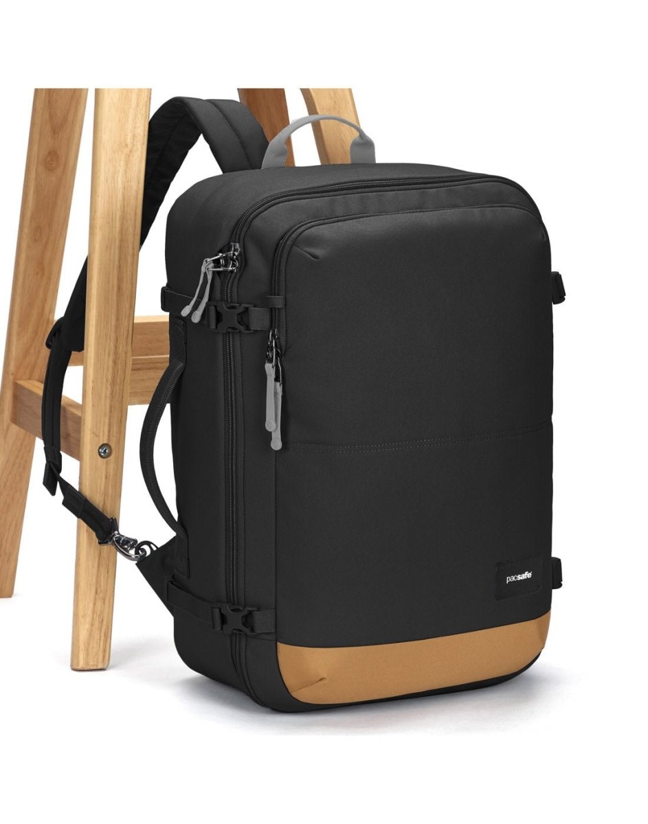 The Pacsafe® GO 34L Anti-theft Carry-on Backpack by Pacsafe, in black/brown recycled polyester, rests by a stool.