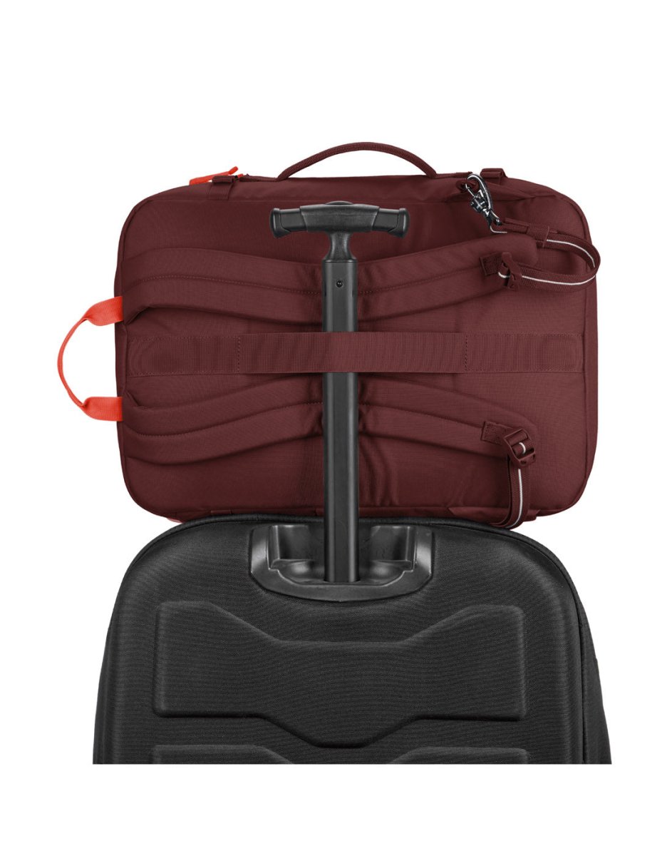 The Pacsafe® GO 34L maroon backpack is attached to a suitcase handle for easy travel.