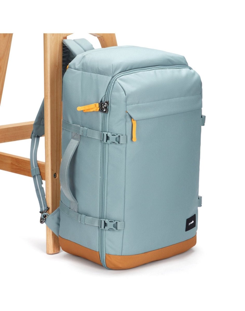 The Pacsafe® GO 44L Anti-theft Carry-on Backpack in light blue with tan accents stands by a wooden chair.