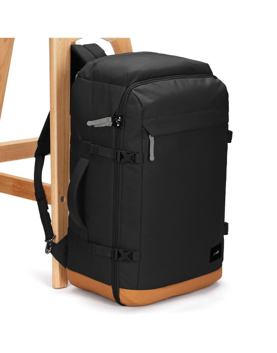 A Pacsafe® GO 44L black carry-on backpack with RFID pocket leans against a wooden chair.