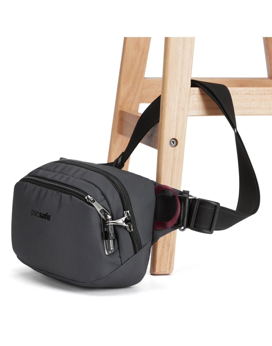 Pacsafe V Anti-theft Hip Pack by Pacsafe with lockable zips & buckle strap, hanging on a wooden chair.