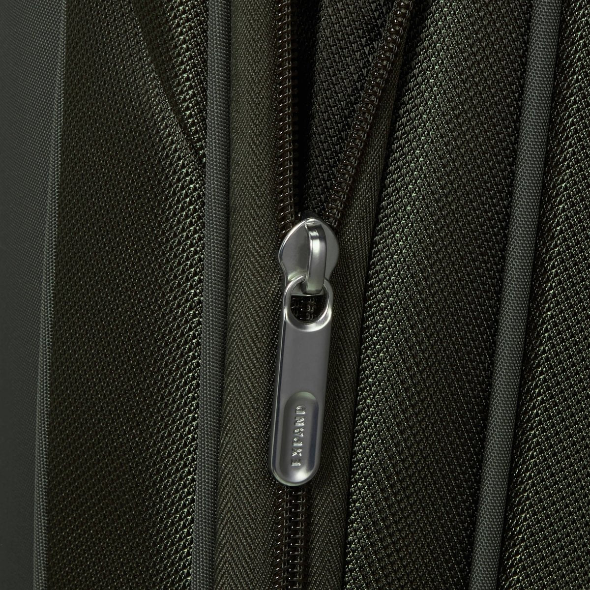 Close-up of a suitcase zipper with "Samsonite" pull tab on textured, dark Samsonite Re-Lite Spinner Medium fabric.