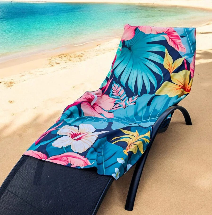A K5 Microfibre Beach Towel sits on sandy beach near turquoise water.