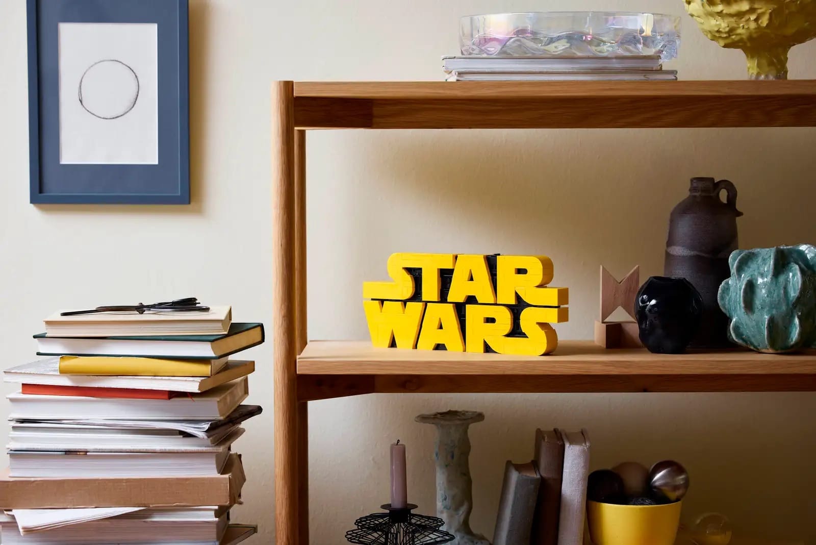 Wooden shelf with books, ceramics, and LEGO® Brick-Built Star Wars™ Logo; framed art and stacked books nearby.