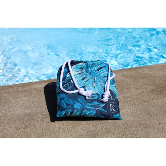 Product Image – A folded K5 XXL Microfibre Beach Towel in blue with white rope straps sits poolside by clear water.