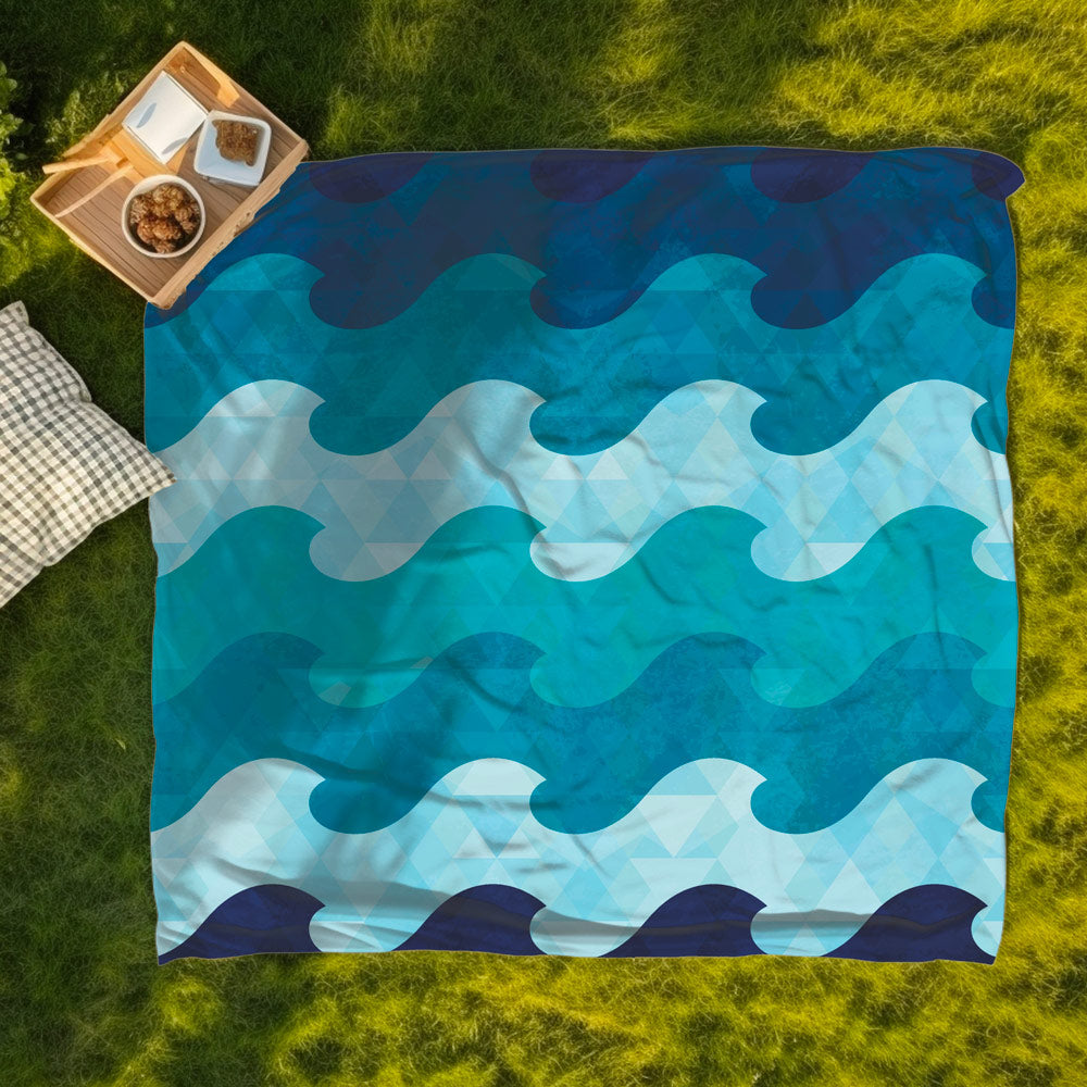 A K5 XXL microfibre beach towel in blue and teal is laid on grass next to snacks and a checked pillow.
