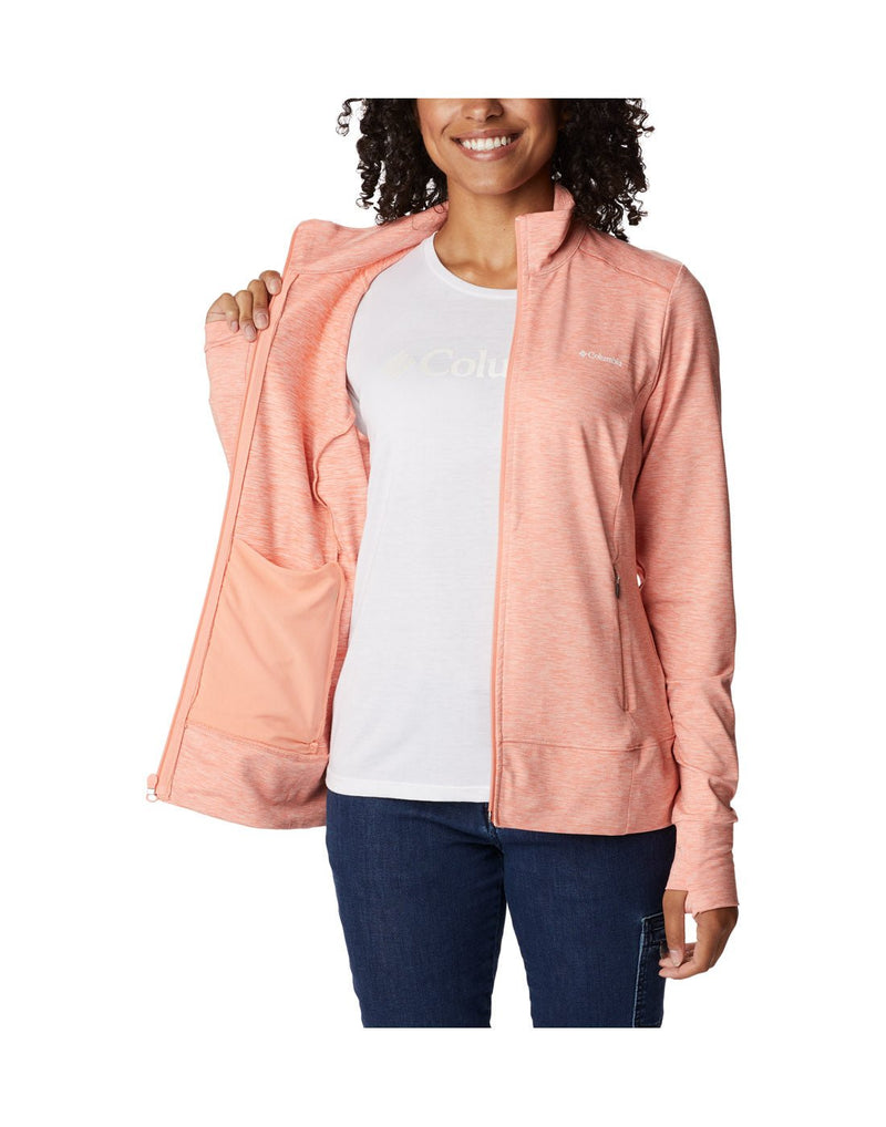 Woman wearing blue jeans, white t-shirt and Columbia Women's Weekend Adventure™ Full Zip Jacket in peach heather, unzipped, holding one side open to show interior, front view