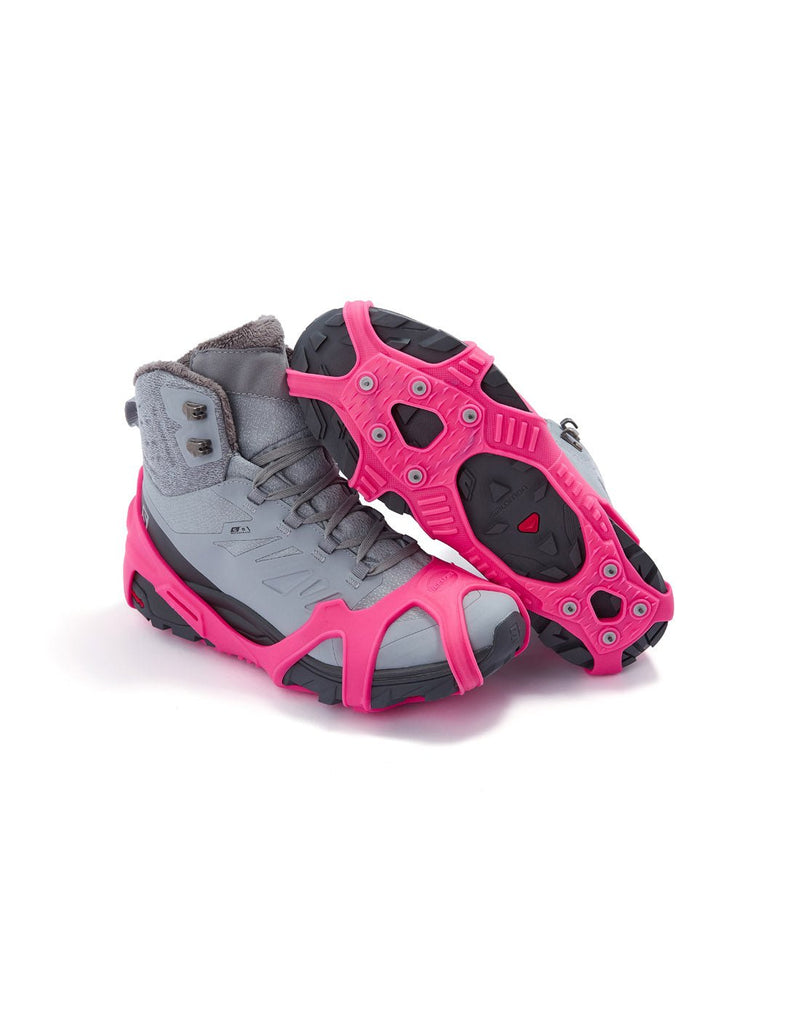 Icetrax V3 Tungsten Ice Cleats in bright pink on a pair of grey hiking boots, side view, one boot is upturned to show bottom cleats