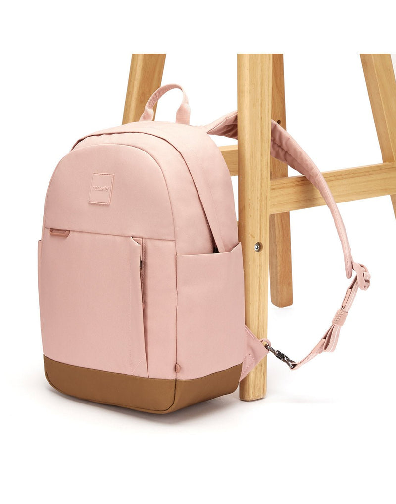 Pacsafe® Go 15L Anti-theft Backpack, sunset pink with tan bottom gusset, with one strap secured to chair leg
