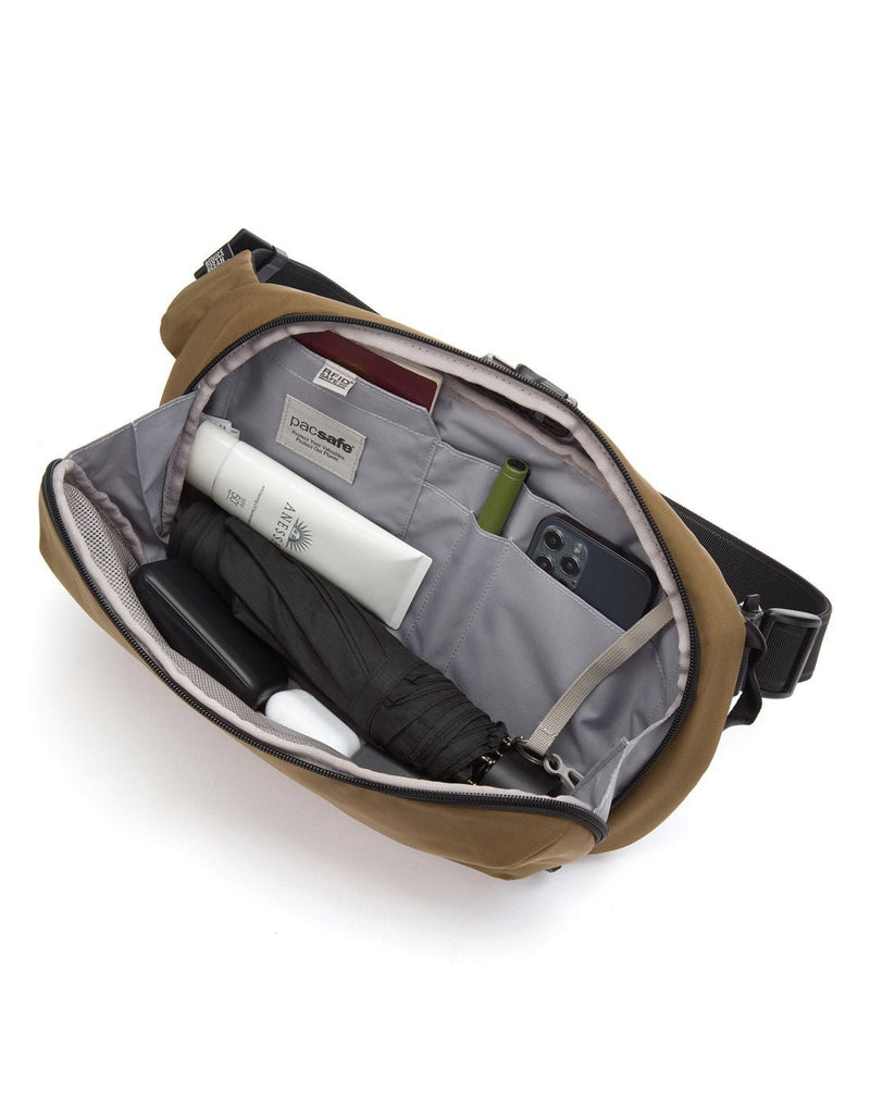 Pacsafe Metrosafe X Anti-Theft Urban Sling, tan, unzipped and open showing phone, pen, passport, tube of cream and small umbrella inside