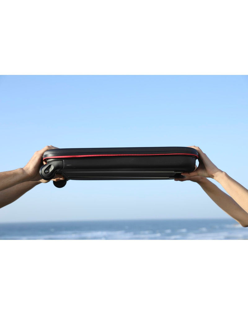 Two people's hands holding either side of the Rollink Flex Earth 20" Carry-On, folded