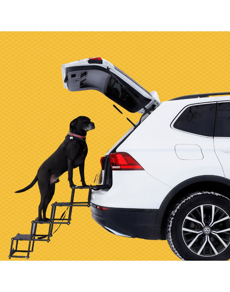 Image of a white SUV with back hatch open and with a fully extended The Good Dog Car Stairs attached. A larger black dog is climbing the stairs into the back of the SUV