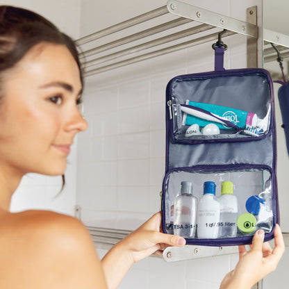 A woman in a bathroom holds a Travelon Wet/Dry 1 Quart Bag with Bottles and Jars, neatly organized inside.