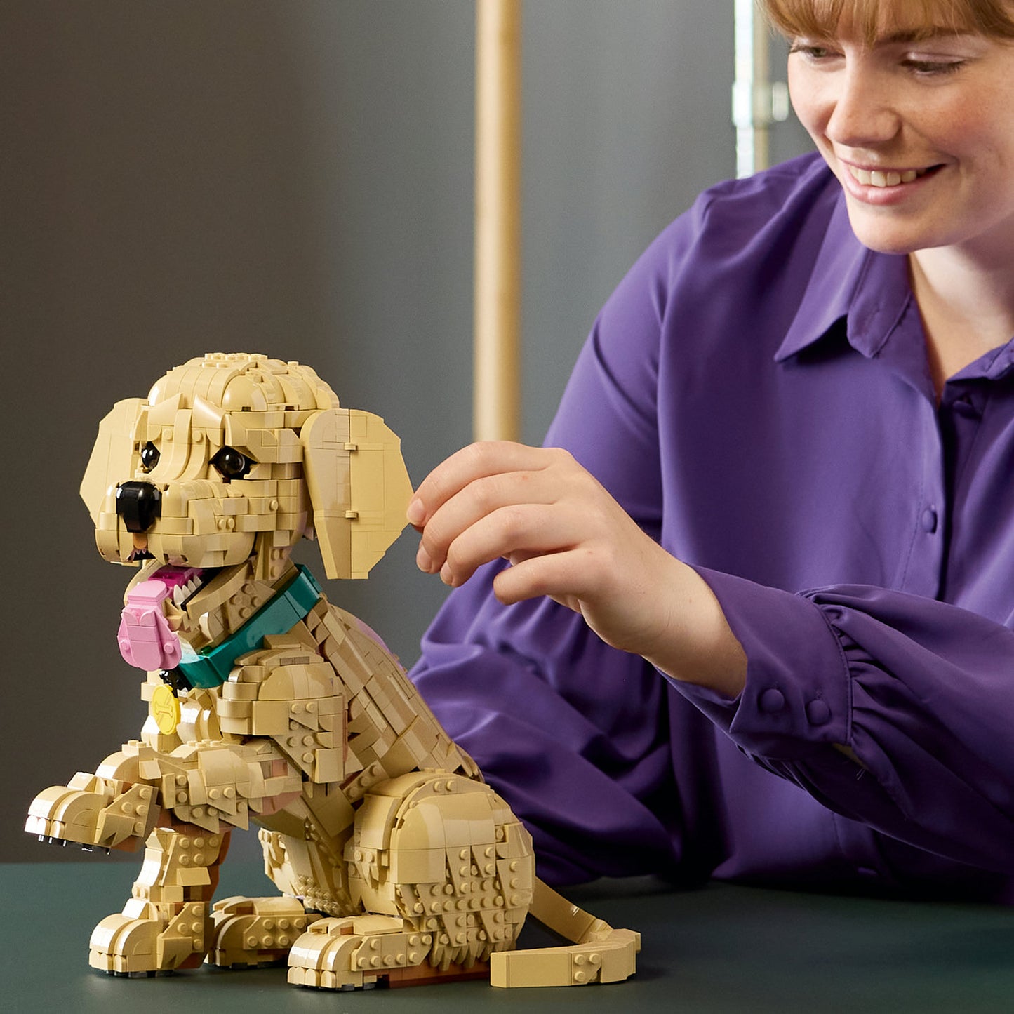 Person in a purple shirt building the LEGO® Golden Retriever Puppy (ONLINE ONLY) by LEGO on a table.