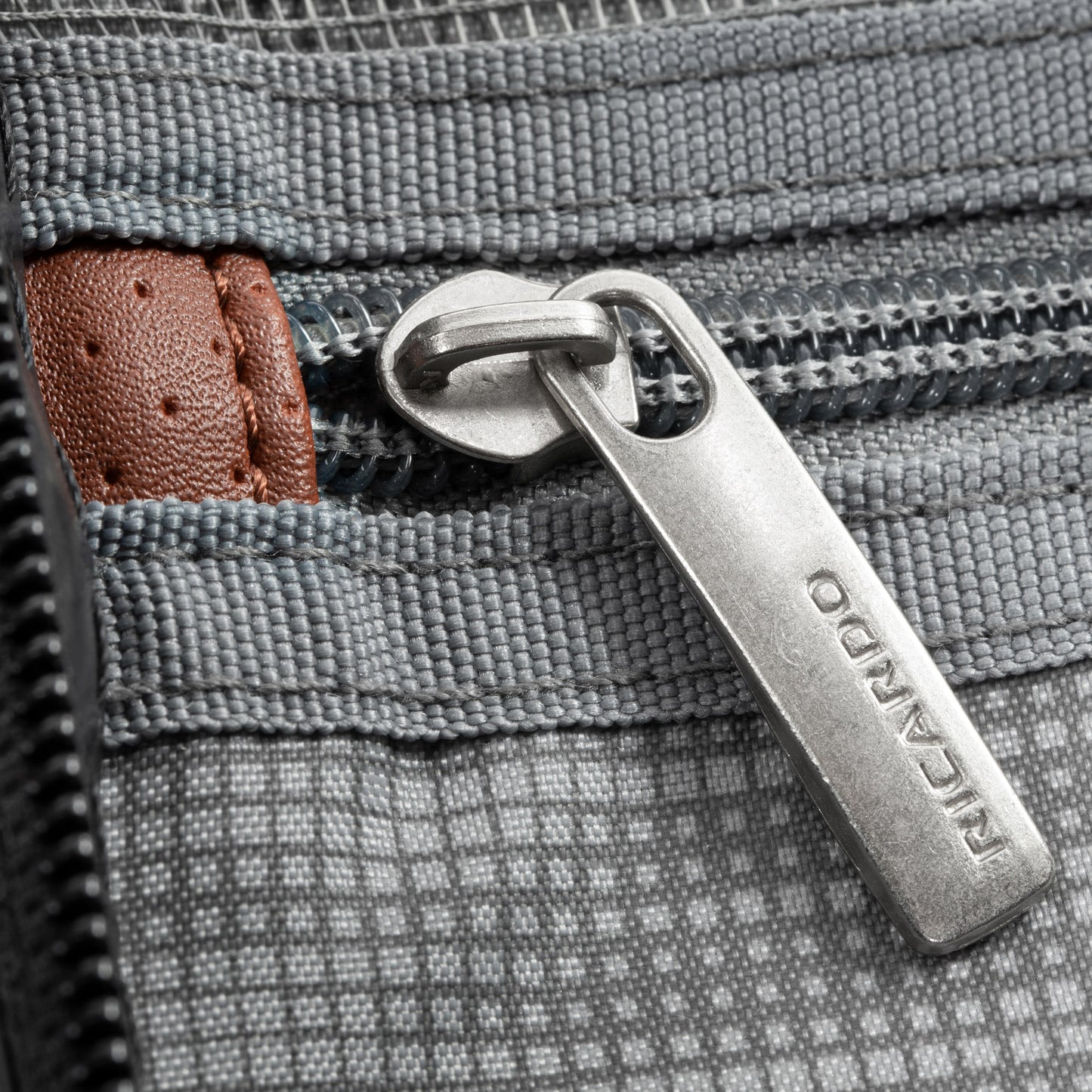 Close-up of a metal zipper on the Ricardo Beverly Hills Montecito 2.0 gray carry-on with brown accent.