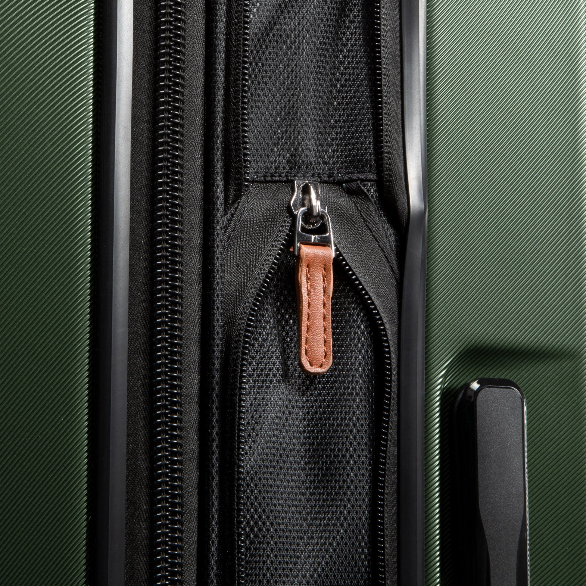 Close-up of a Ricardo Beverly Hills Montecito 2.0 green hardside spinner with black zipper, brown pull tab, expandable storage.