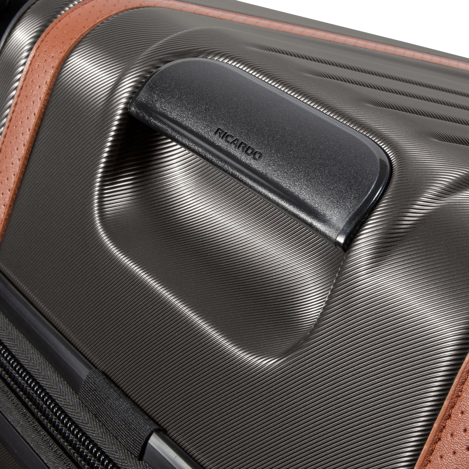 Close-up of Ricardo Beverly Hills black Montecito 2.0 hardside suitcase with textured surface, brown accent, and handle.