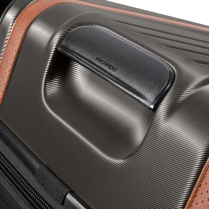 Close-up of Ricardo Beverly Hills black Montecito 2.0 hardside suitcase with textured surface, brown accent, and handle.