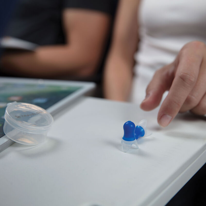 Hands grabbing one of the blue Travelon Pressure Reducing Earplugs which is on an airplane tray