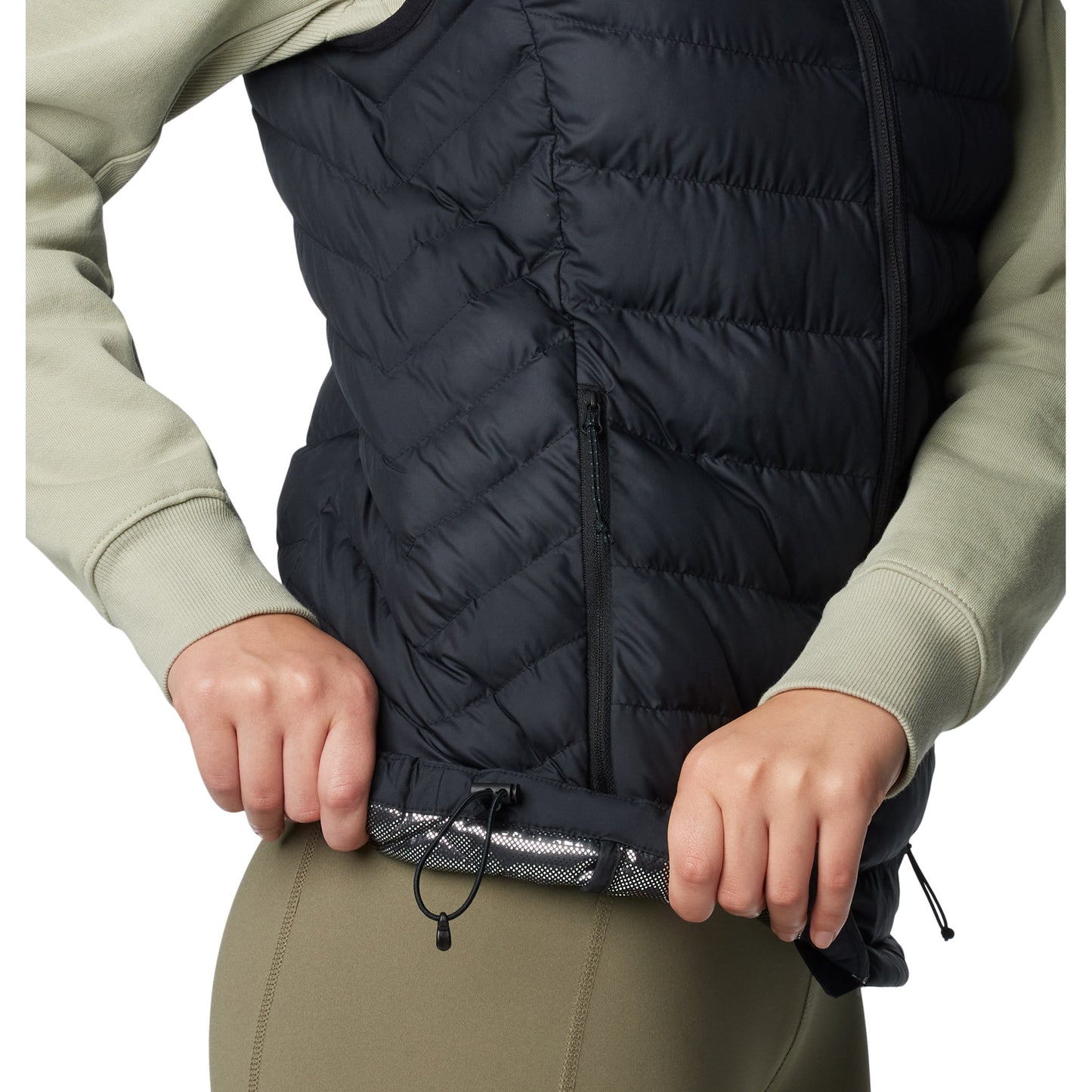 Bottom half of woman wearing Columbia Women's Powder Lite™ II Vest in black, side view, holding bottom hem up to show omni-heat silver lining