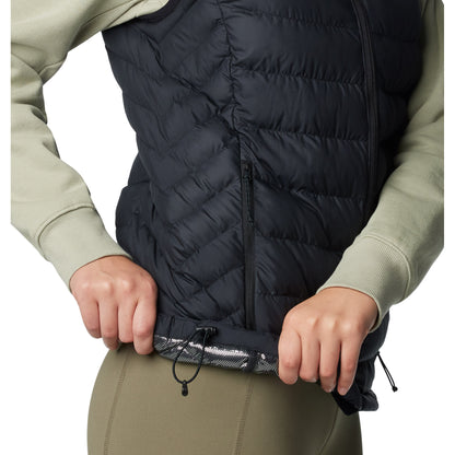 Bottom half of woman wearing Columbia Women's Powder Lite™ II Vest in black, side view, holding bottom hem up to show omni-heat silver lining