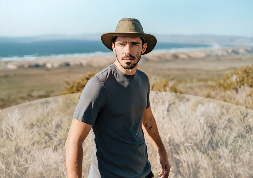 Man in Tilley hat with large shore in the background looking into the distance. 