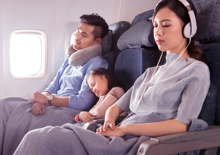 Family of three: mom, dad and young daughter comfortably resting on a flight in their row of seats.