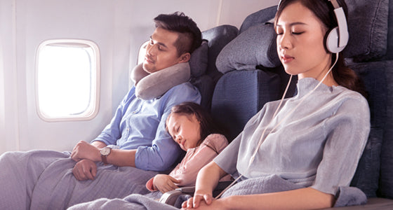 Family of three: mom, dad and young daughter comfortably resting on a flight in their row of seats.