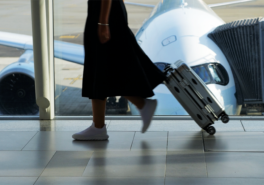 Image showing woman walking at an airport, rolling her carry-on with plane parked at a gate.