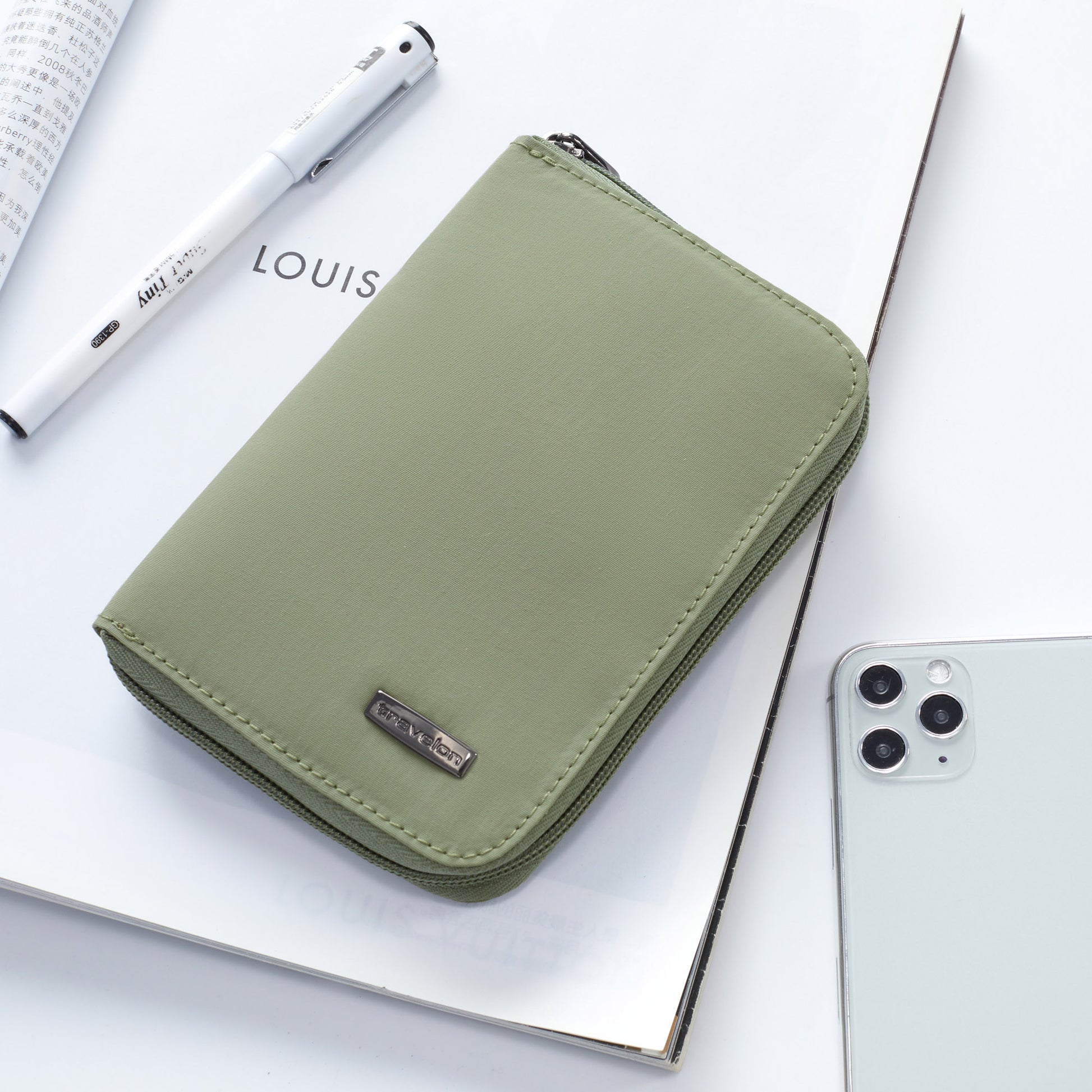 A green Travelon RFID Blocking Zip Passport Wallet and a white pen sit with a smartphone on an open magazine.
