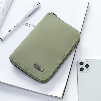 A green Travelon RFID Blocking Zip Passport Wallet and a white pen sit with a smartphone on an open magazine.