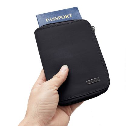 A hand holds the Travelon RFID Blocking Zip Passport Wallet (ONLINE ONLY) with a passport inside against a white background.