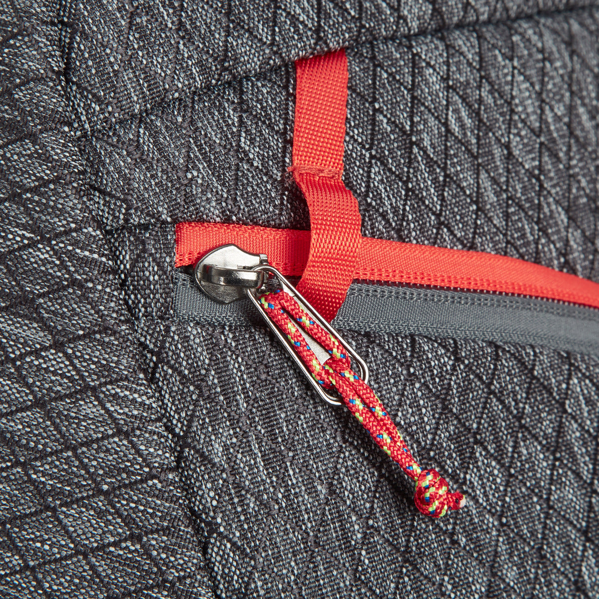 Close-up of a red zipper on Travelon's gray fabric, featuring Greenlander's anti-theft security cord pull loop.