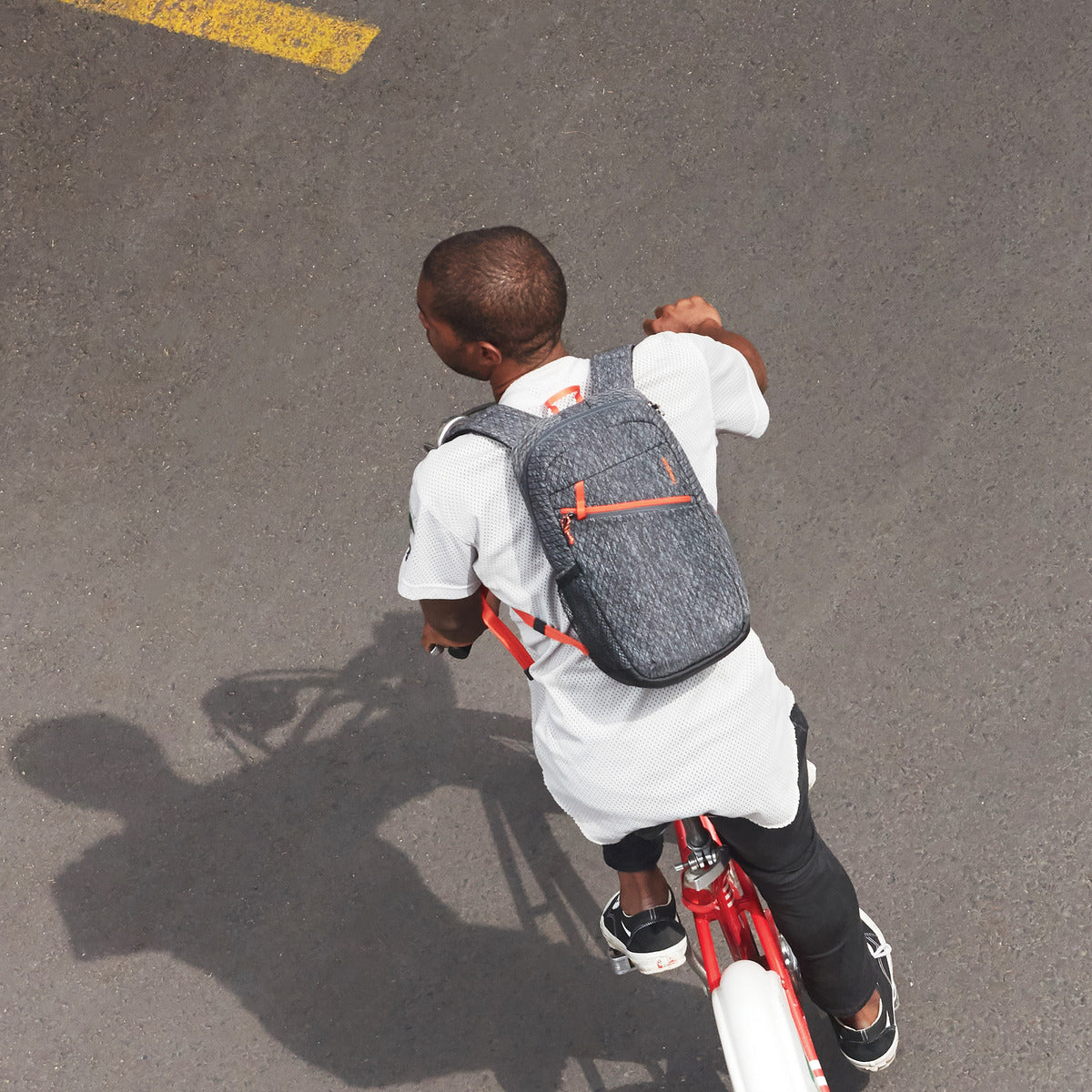 A Greenlander rides a red bike, wearing a white shirt and a gray Travelon Anti-Theft 9L Backpack.