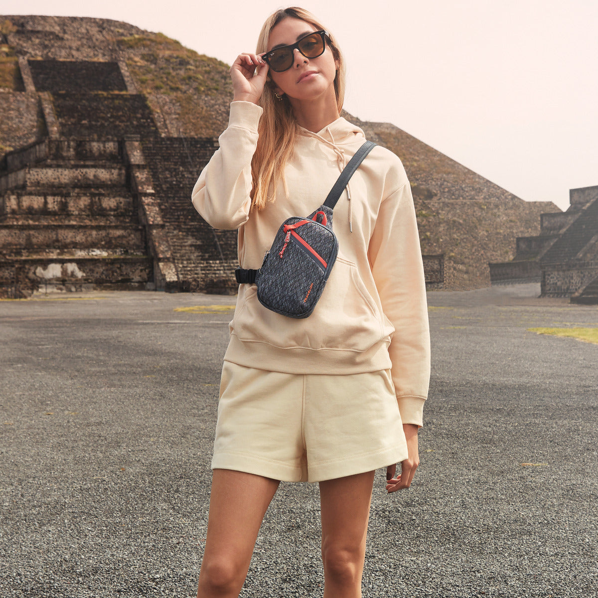 A person wears a Travelon Anti-Theft Greenlander Sling outdoors, with stone stairs in the background.