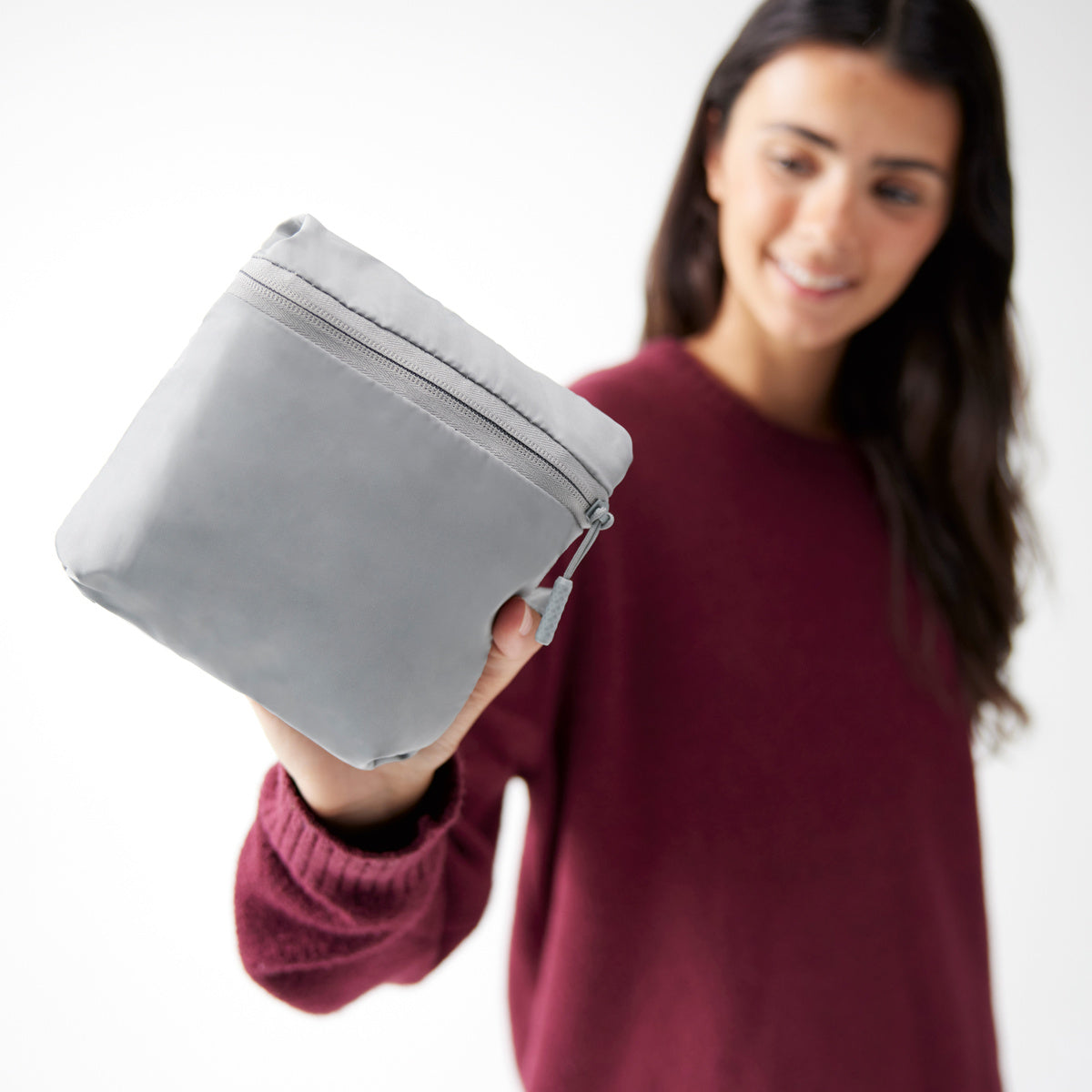 Woman holding the graphite Travelon Pi Daily Carry Tote folded into itself in a small zippered pouch