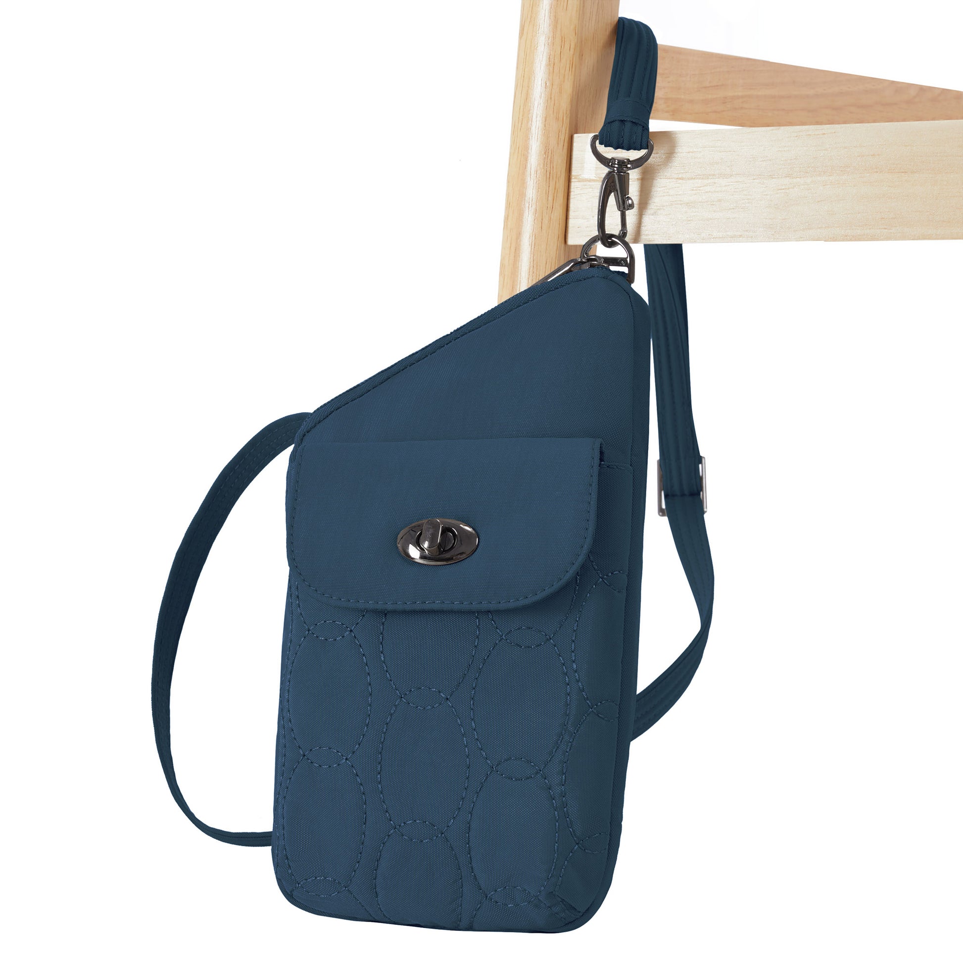 The Travelon Runways Anti-theft Slim Asymmetric Crossbody hangs neatly from a light wooden chair.