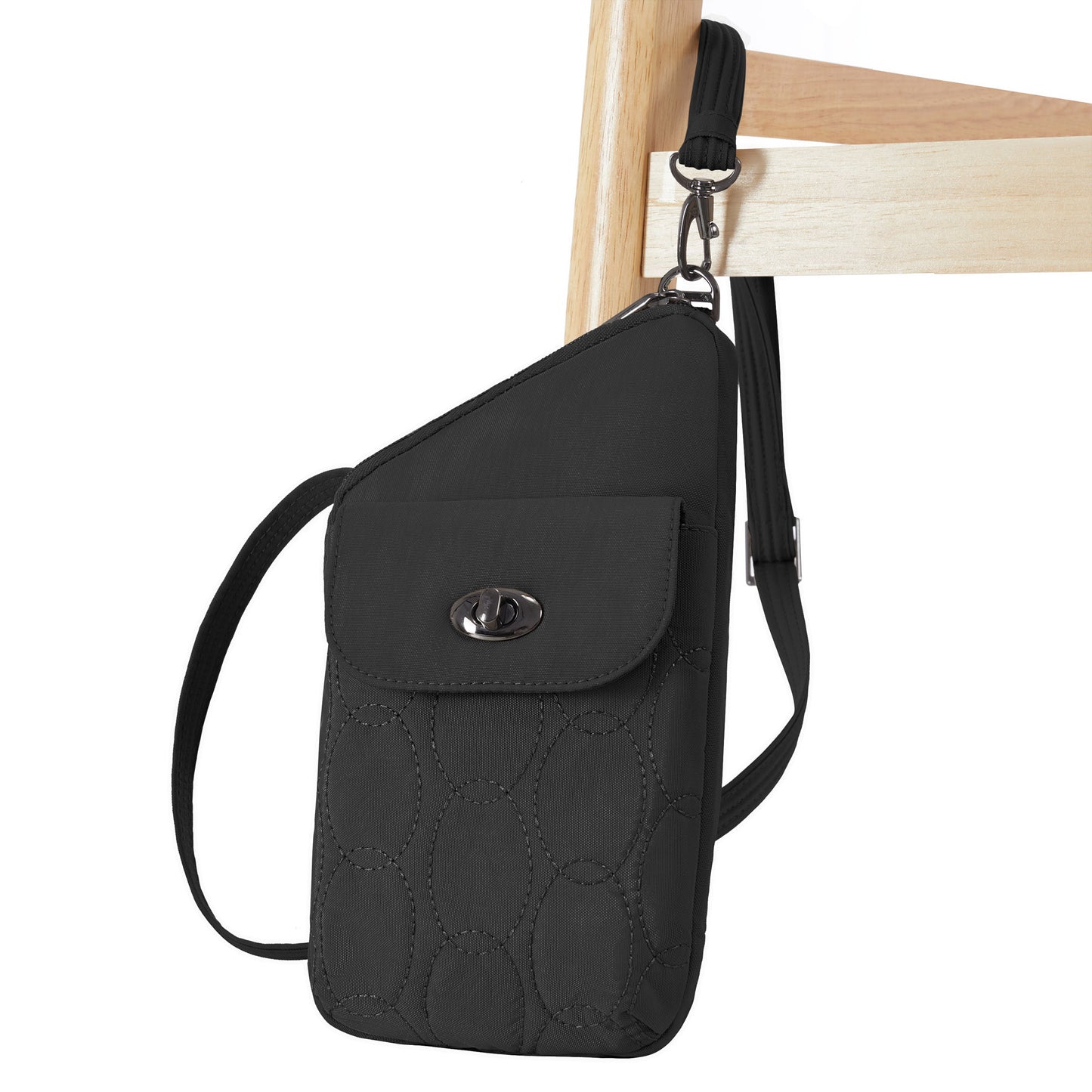 The Travelon Runways Anti-theft Slim Asymmetric Crossbody hangs from the back of a wooden chair.