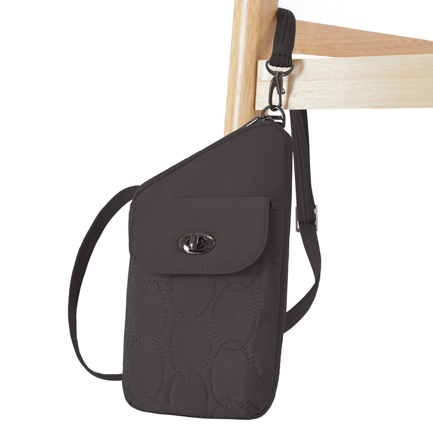 The Travelon Runways Anti-theft Slim Asymmetric Crossbody hangs from the back of a wooden chair.