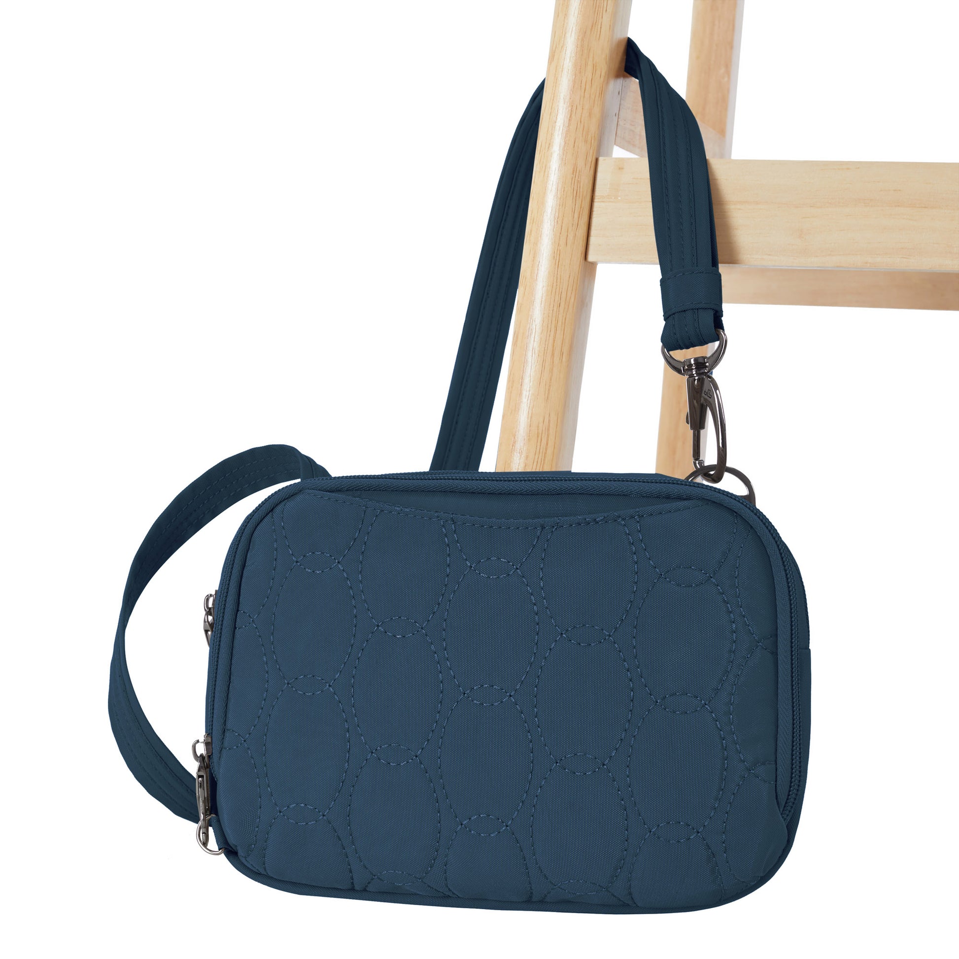 The Travelon Runways Anti-theft Double Compartment Crossbody in dark blue hangs on a wooden chair.