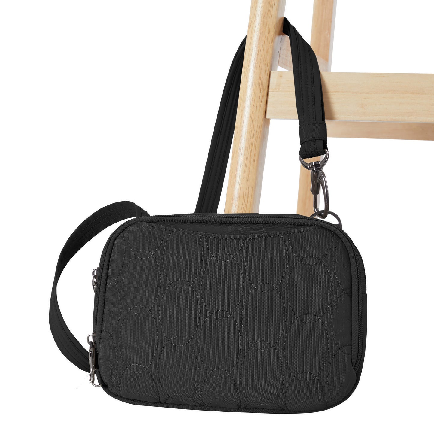 The Travelon Runways Anti-theft Double Compartment Crossbody in black quilted style hangs on a wooden chair.