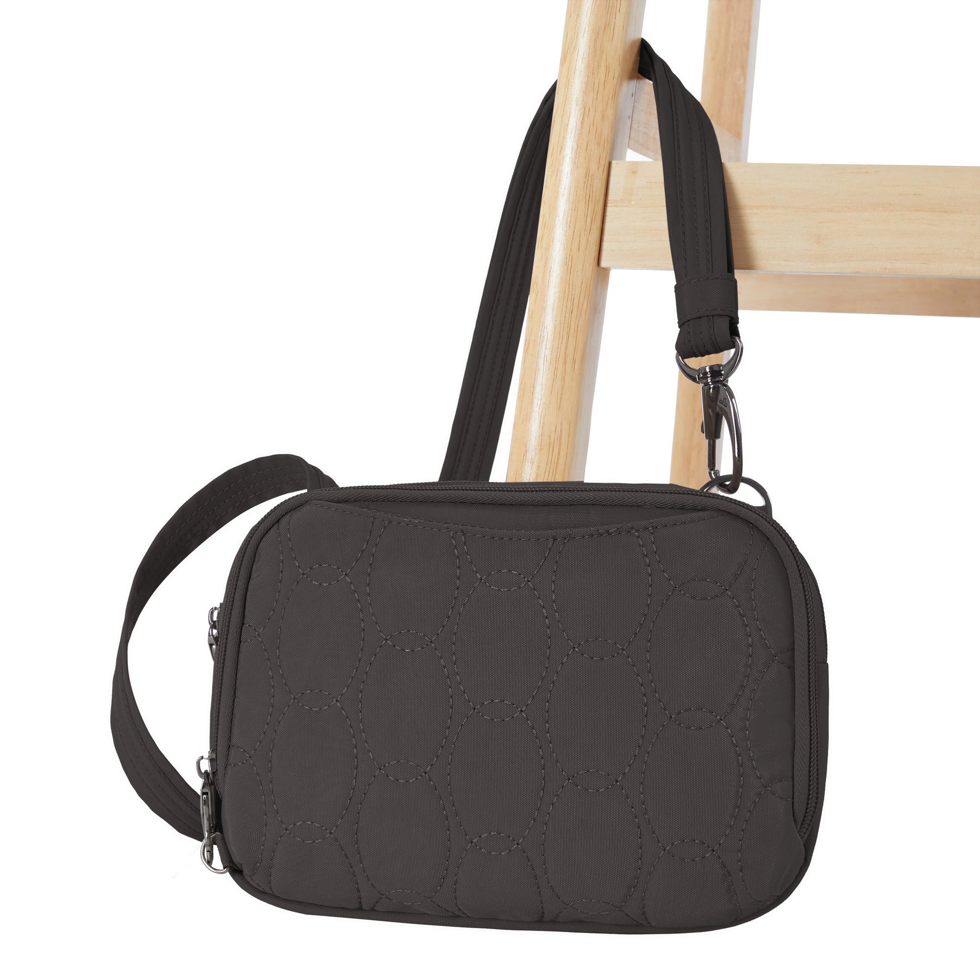 A Travelon Runways Anti-theft Double Compartment Crossbody bag hangs from a wooden chair.