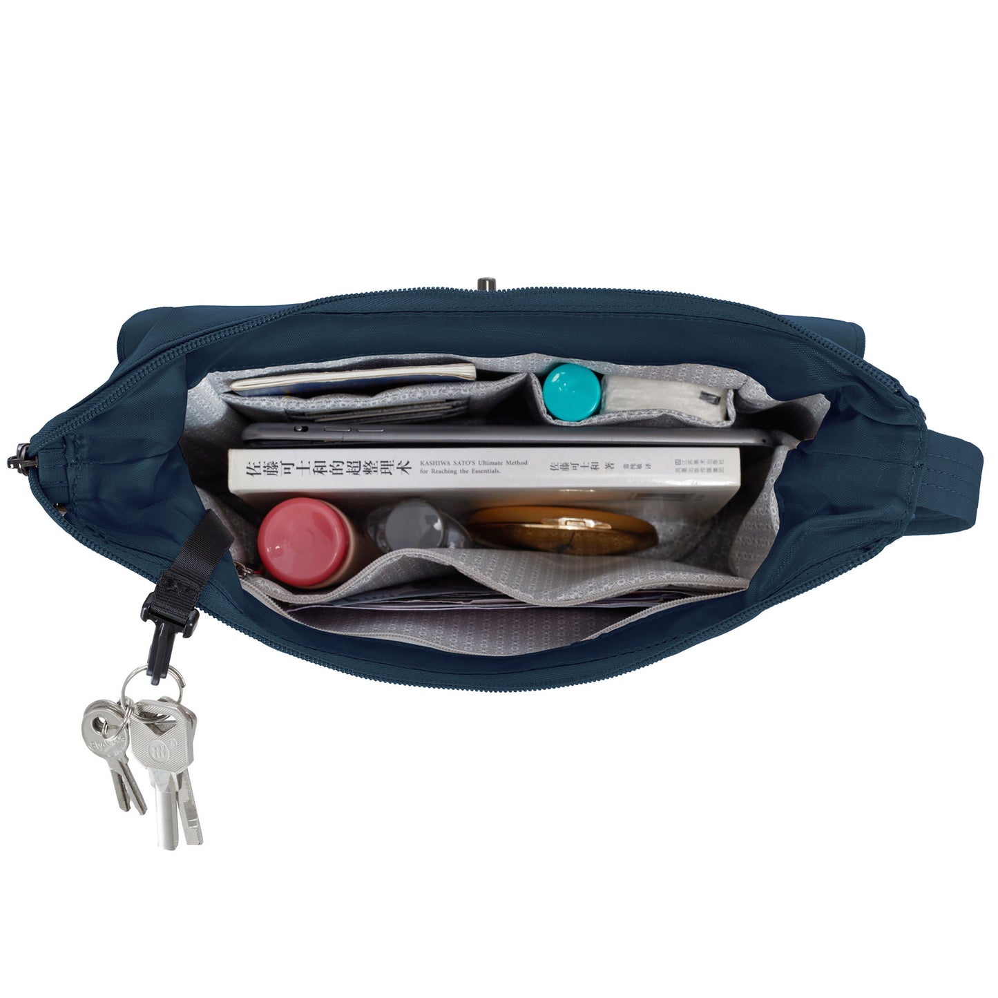 Top view of Travelon Runways Anti-theft Crossbody with books, red bottle, teal container, keys & security features.