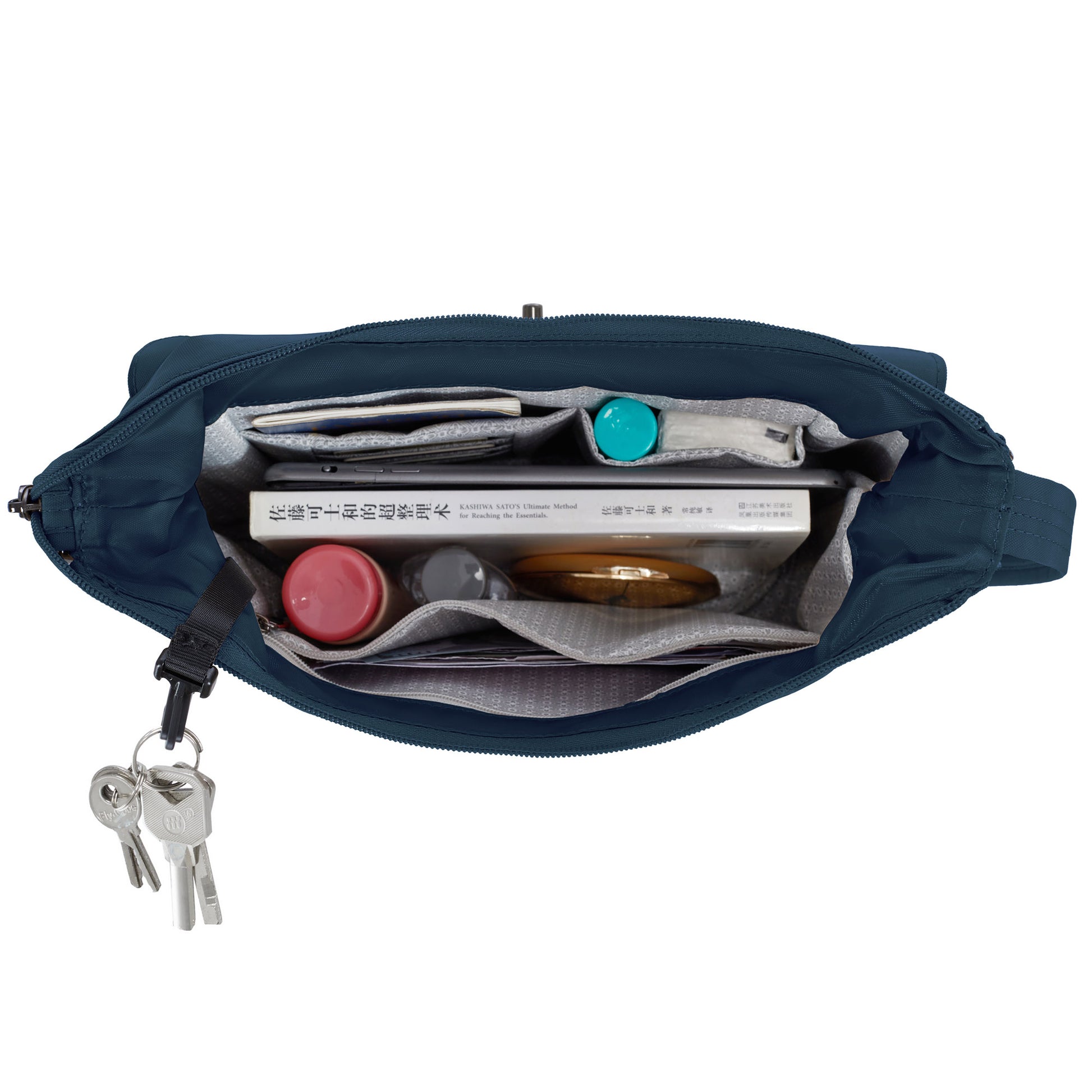 Top view of Travelon Runways Anti-theft Crossbody with books, red bottle, teal container, keys & security features.