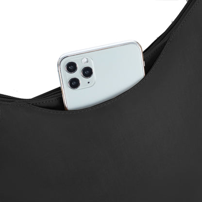 A smartphone with three rear cameras peeks from a Travelon Runways Anti-theft Crossbody against white.