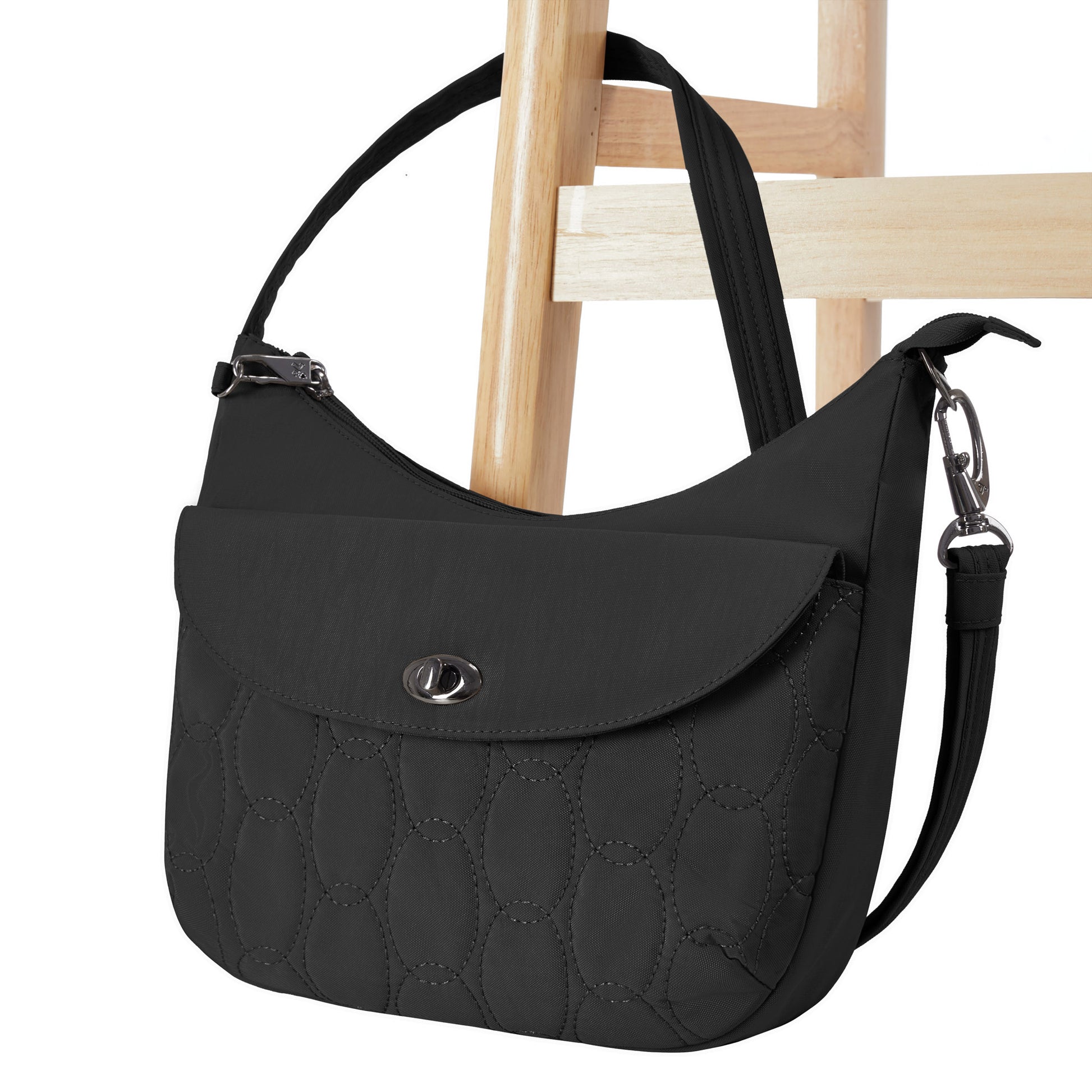Travelon Runways Anti-theft Medium Crossbody by Travelon with flap closure, shown on a wooden chair.