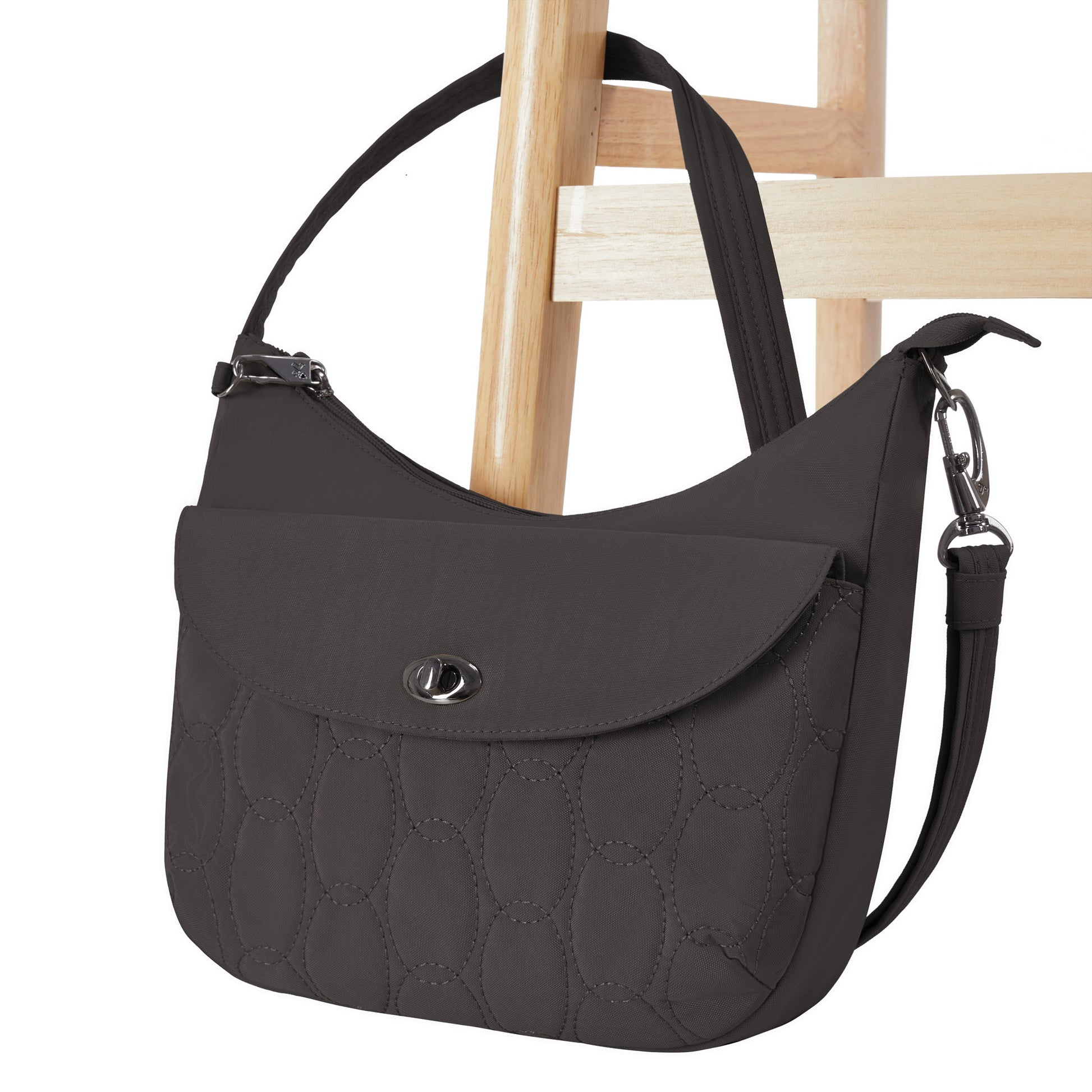 The Travelon Runways Anti-theft Medium Crossbody in black hangs on a wooden chair.
