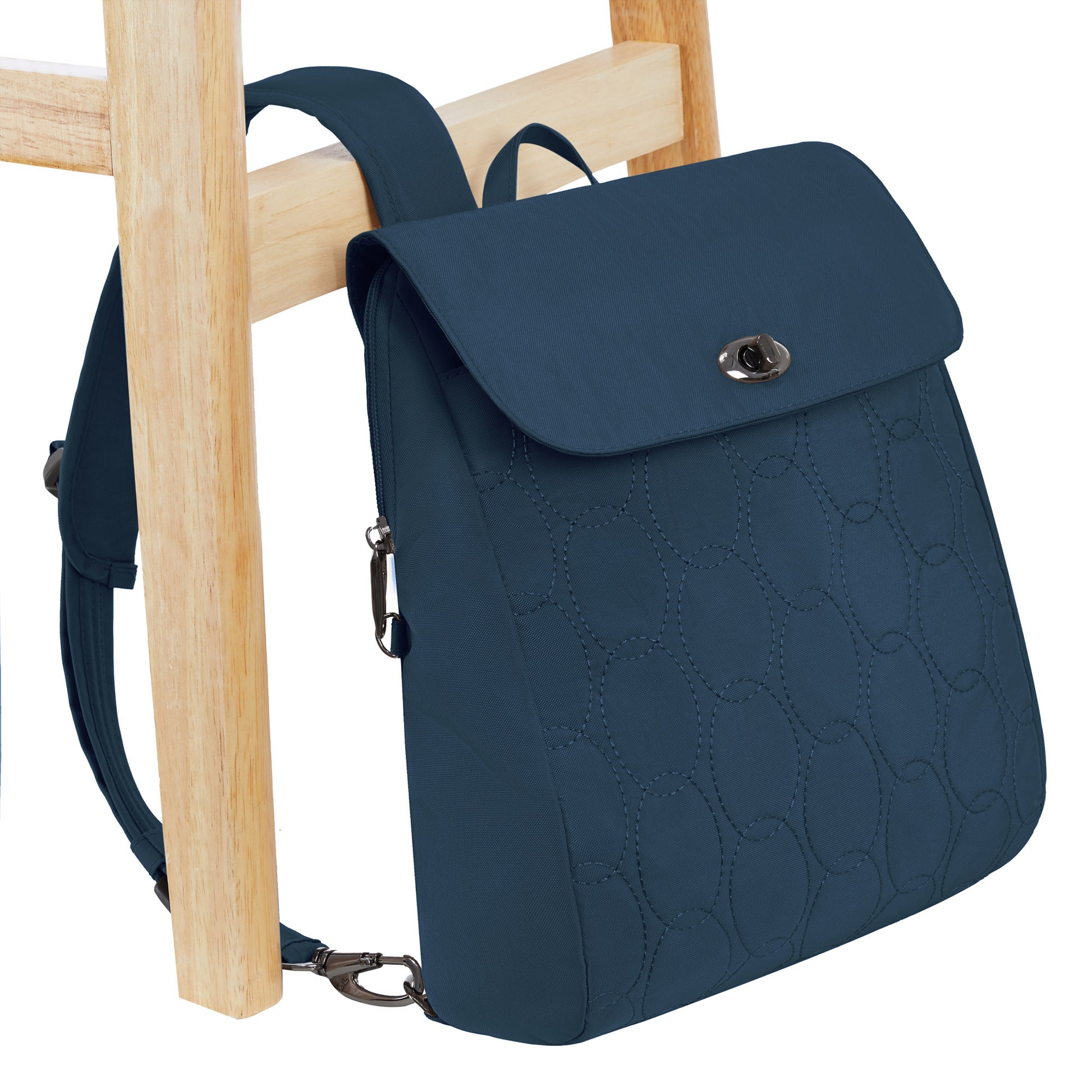 The Travelon Runways Anti-theft Compact Backpack in dark blue hangs on a light wooden chair.